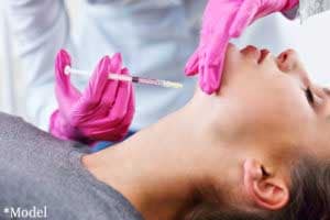 doctor in pink gloves injecting dermal filler into patient's chin for augmentation