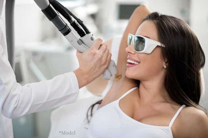 woman in protective glasses receiving laser hair removal on armpit from medical professional