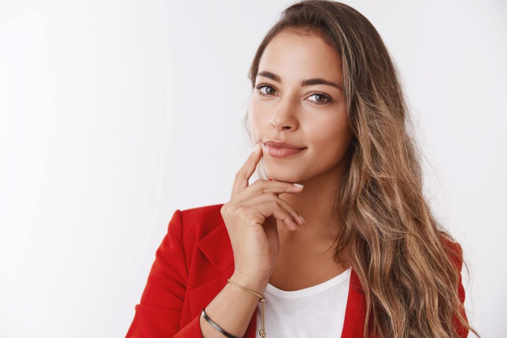 Close up self assured successful rich businesswoman wearing red jacket touching jawline smiling confident looking camera smart intelligent, know how maintain business attract customers