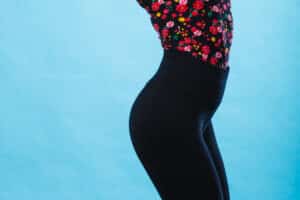 A close up of a woman's body wearing black pants and a floral tucked in blouse in front of a blue background