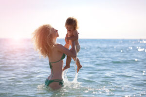 Woman in bikini at the beach holding a child after a mommy make over in San Antonio, TX
