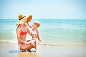 Mother with tight body on beach with her toddler after having a mommy makeover.
